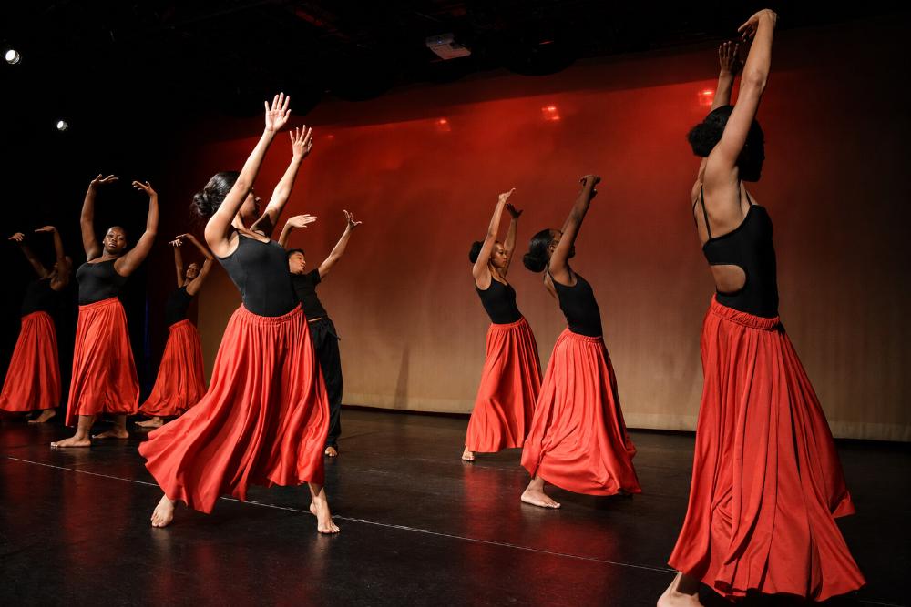 Dancers performing onstage in black tops and flowing red skirts